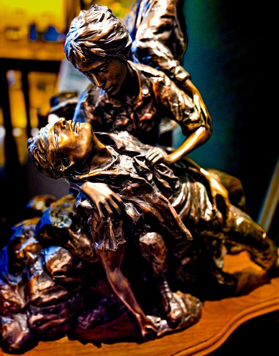 Bronze sculpture depicting one figure cradling another in a scene of mourning